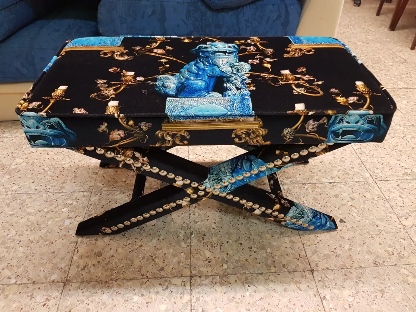 Banqueta tapizada en tela negra con estampado de leones foo azules y tachuelas